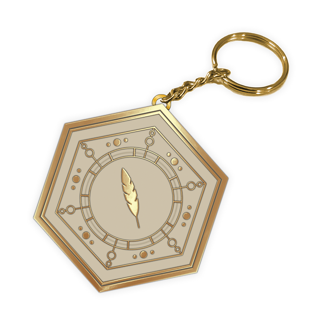 A hexagonal gold-toned keychain featuring an engraved circular dial design with a central feather motif, attached to a gold split ring and chain, shown on a plain white background.