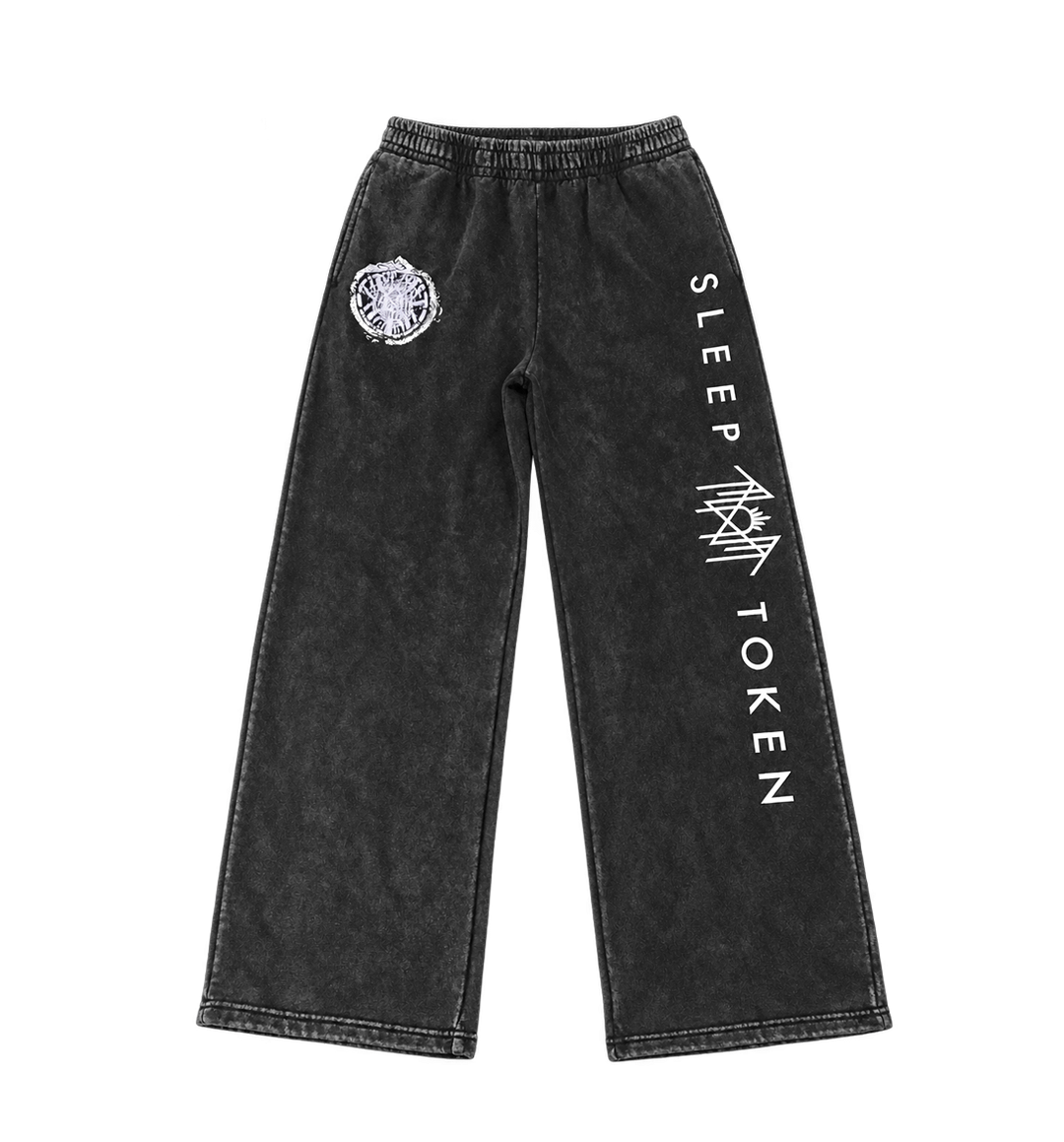 Black acid-wash wide-leg sweatpants featuring a white circular graphic on the left thigh and vertical white text reading 'SLEEP TOKEN' with a geometric logo on the right leg, shown against a plain white background.